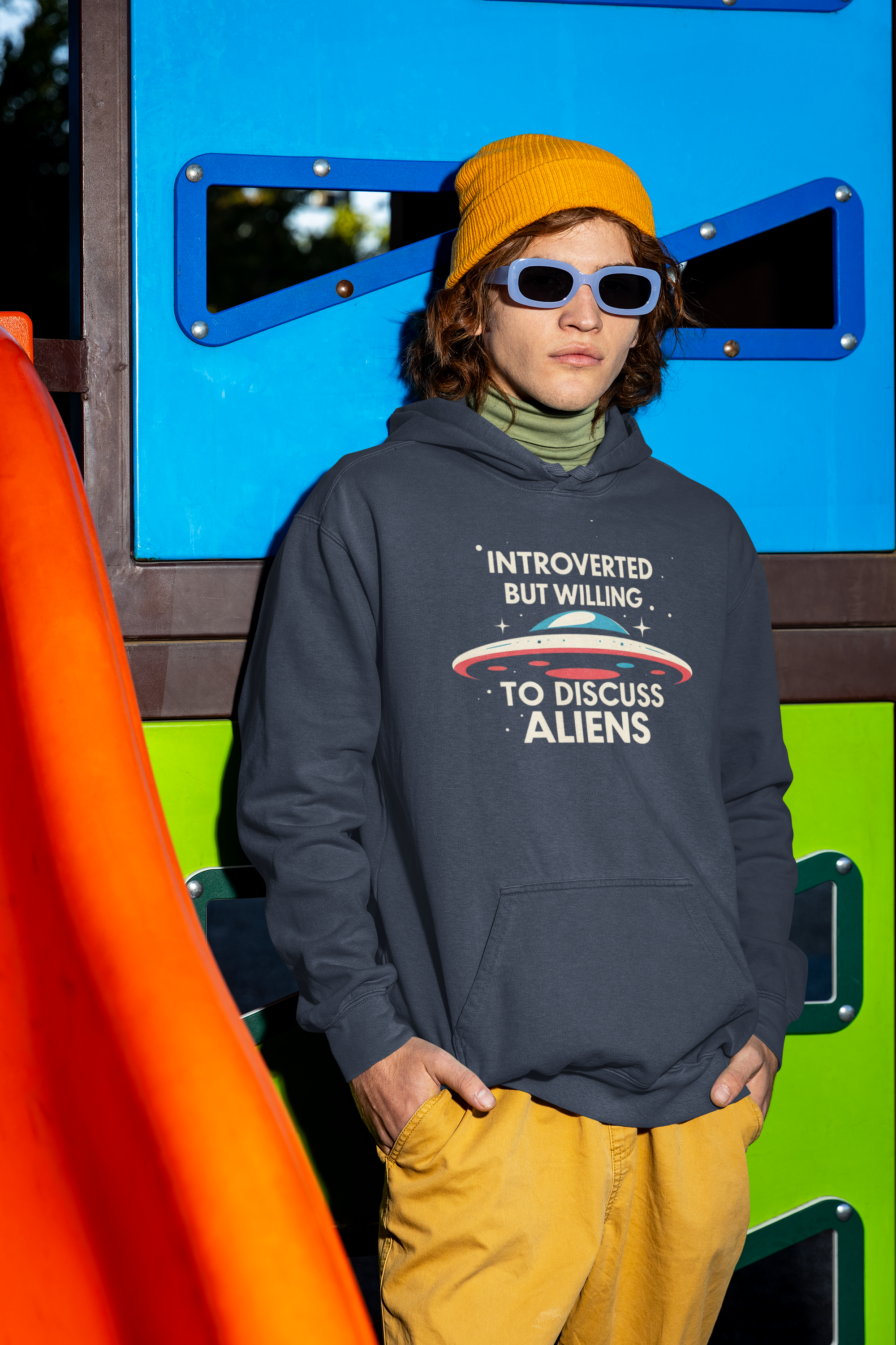 Person wearing a hoodie with text standing in front of colorful playground equipment
