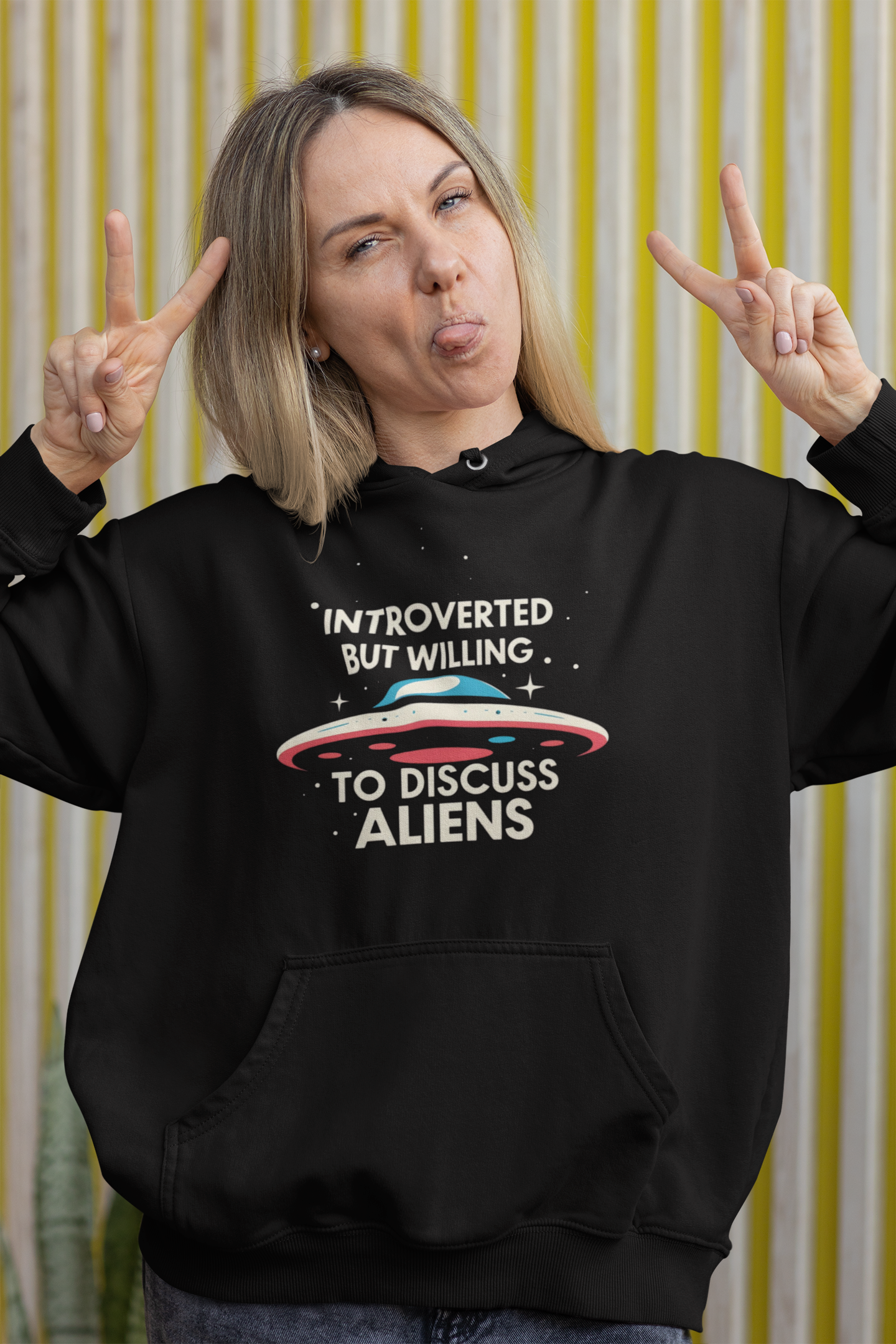 Person wearing a black hoodie with an alien-themed design and text, making peace signs.