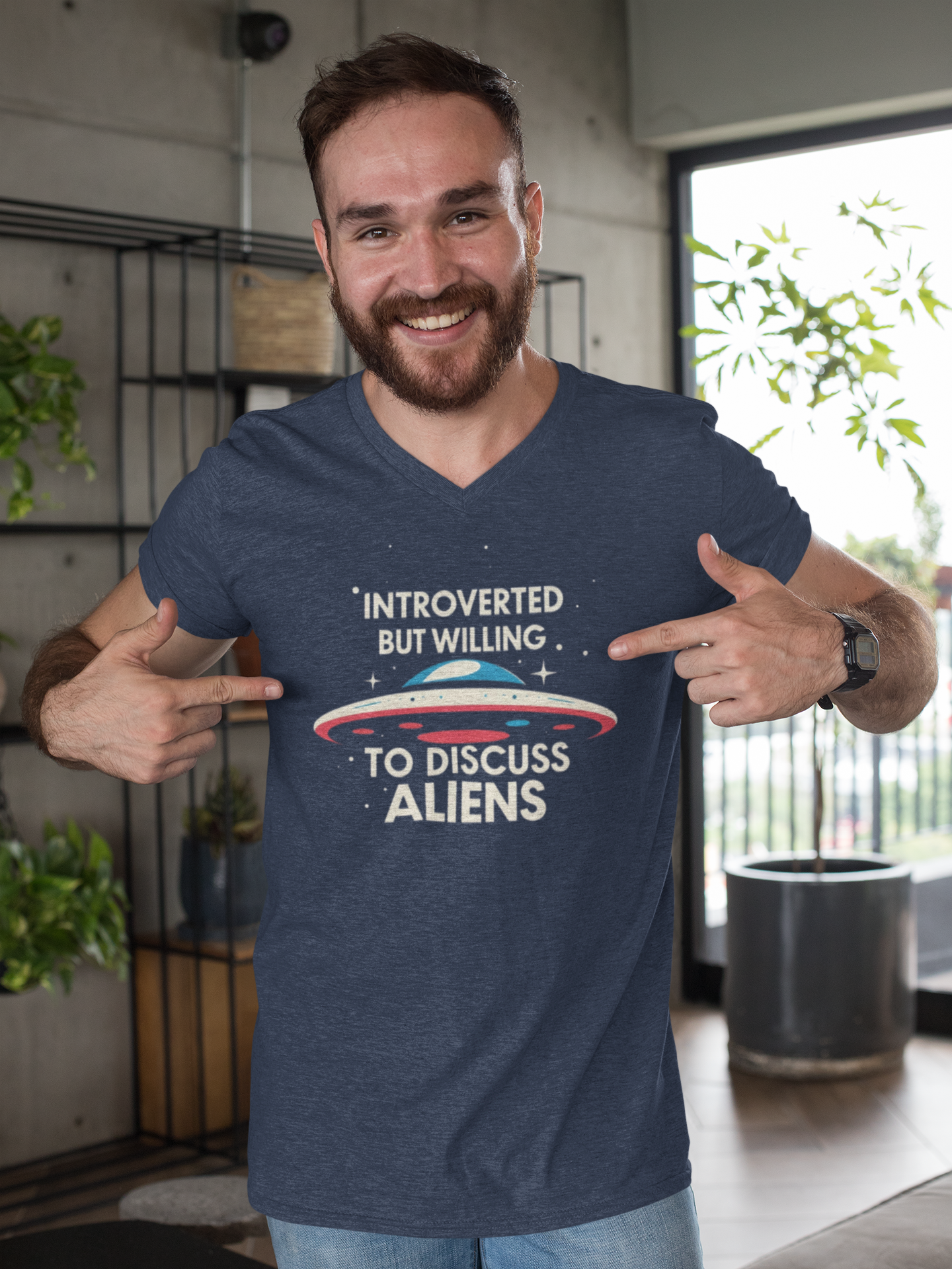 Man wearing a blue t-shirt with an alien graphic and text, pointing at the shirt.