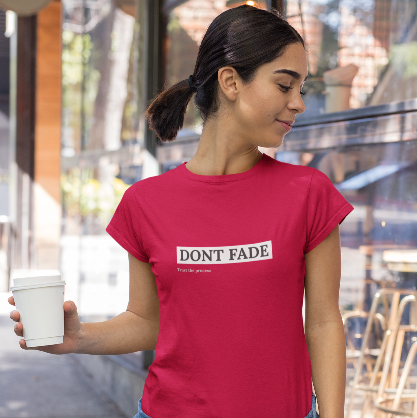 Woman wearing a red t-shirt with 'DON'T FADE' text, holding a coffee cup outdoors.