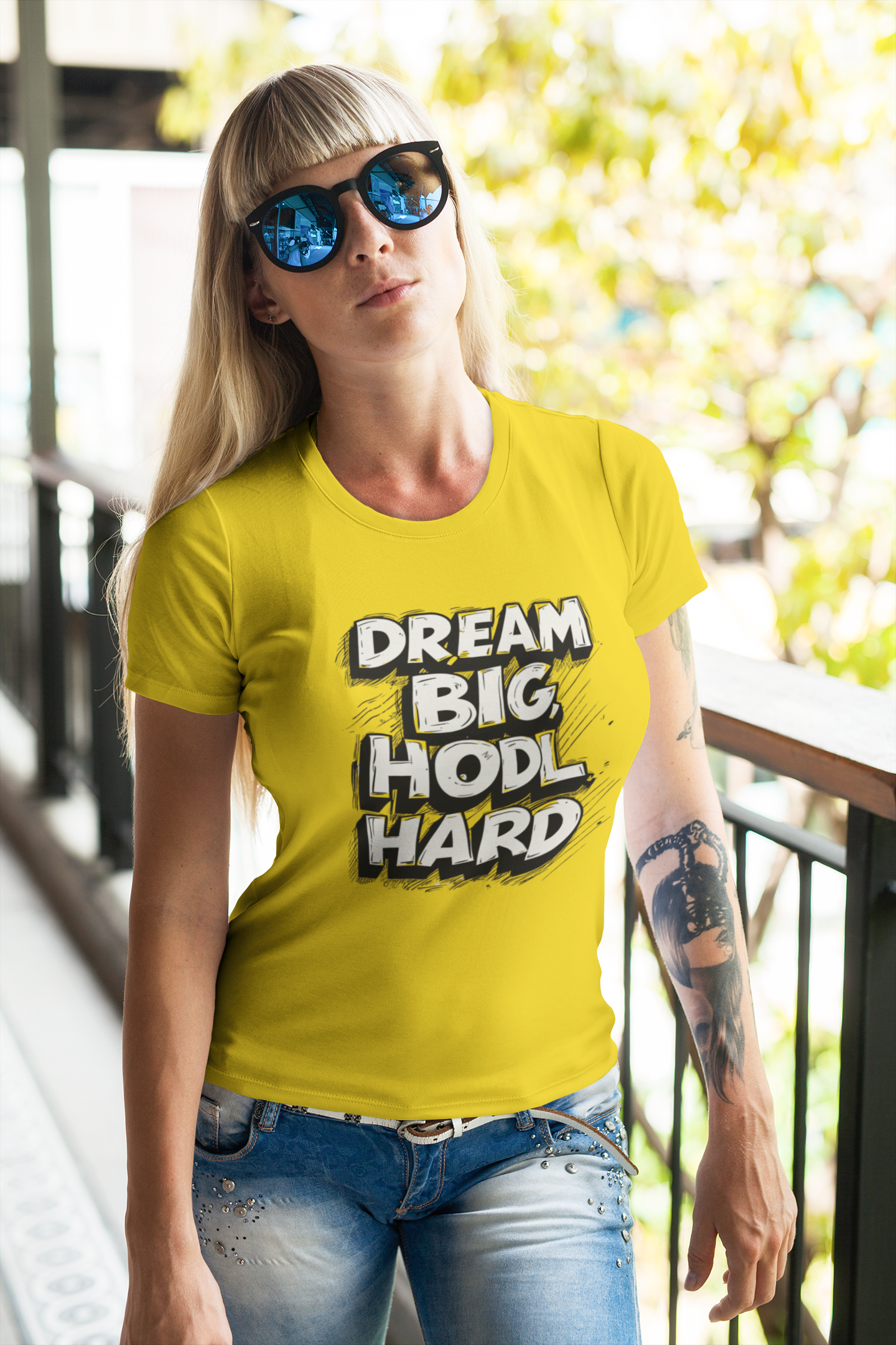 Woman wearing a yellow t-shirt with 'Dream Big Hodl Hard' text, standing outdoors.