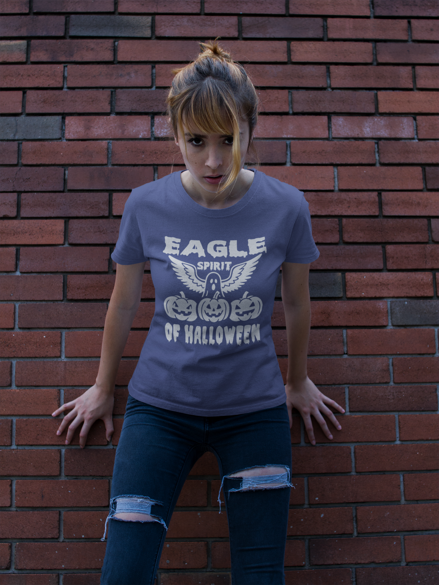 Person wearing a blue t-shirt with 'Eagle Spirit of Halloween' design against a brick wall.