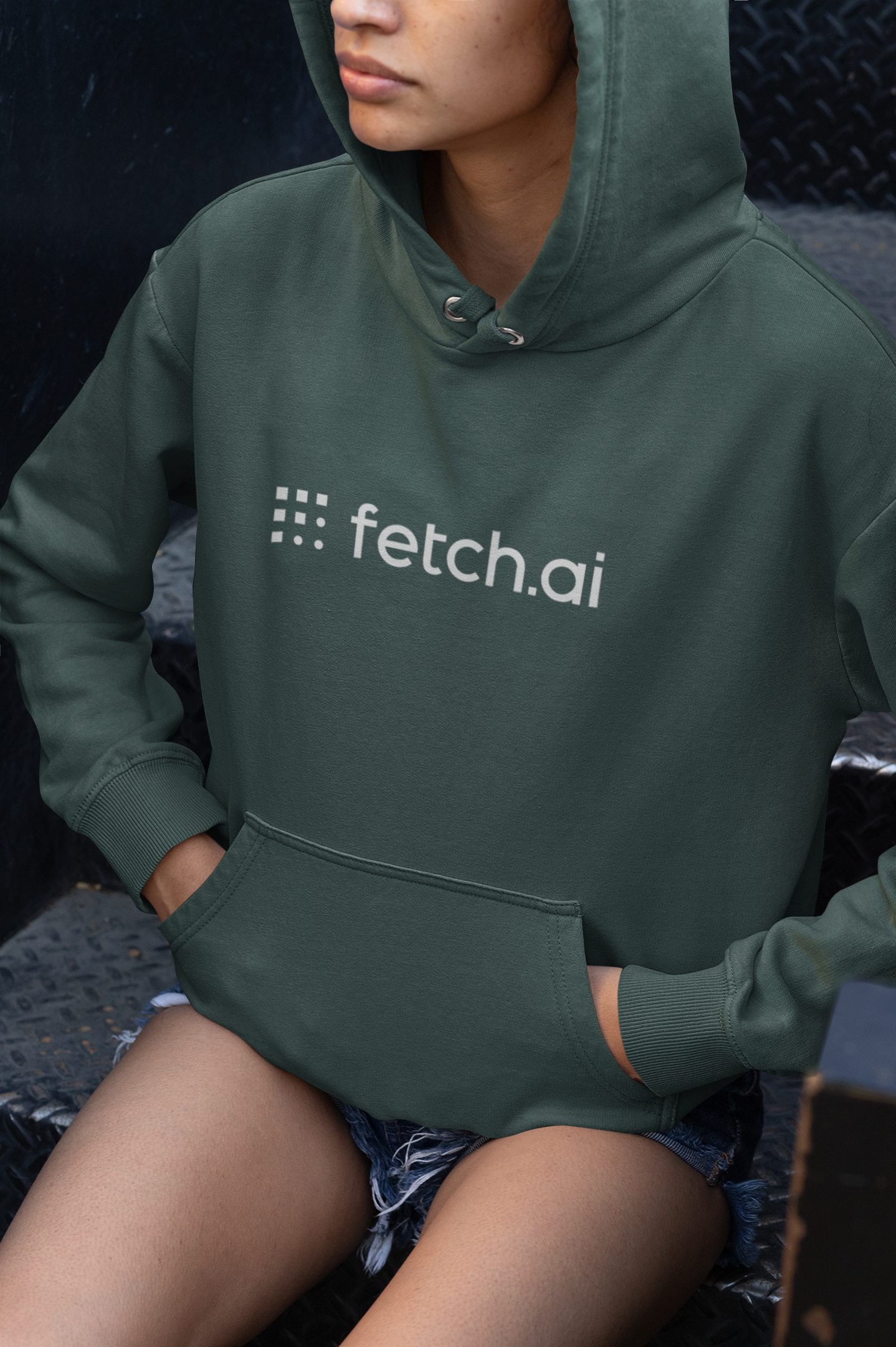 Person wearing a green hoodie with 'fetch.ai' logo sitting on a textured surface.