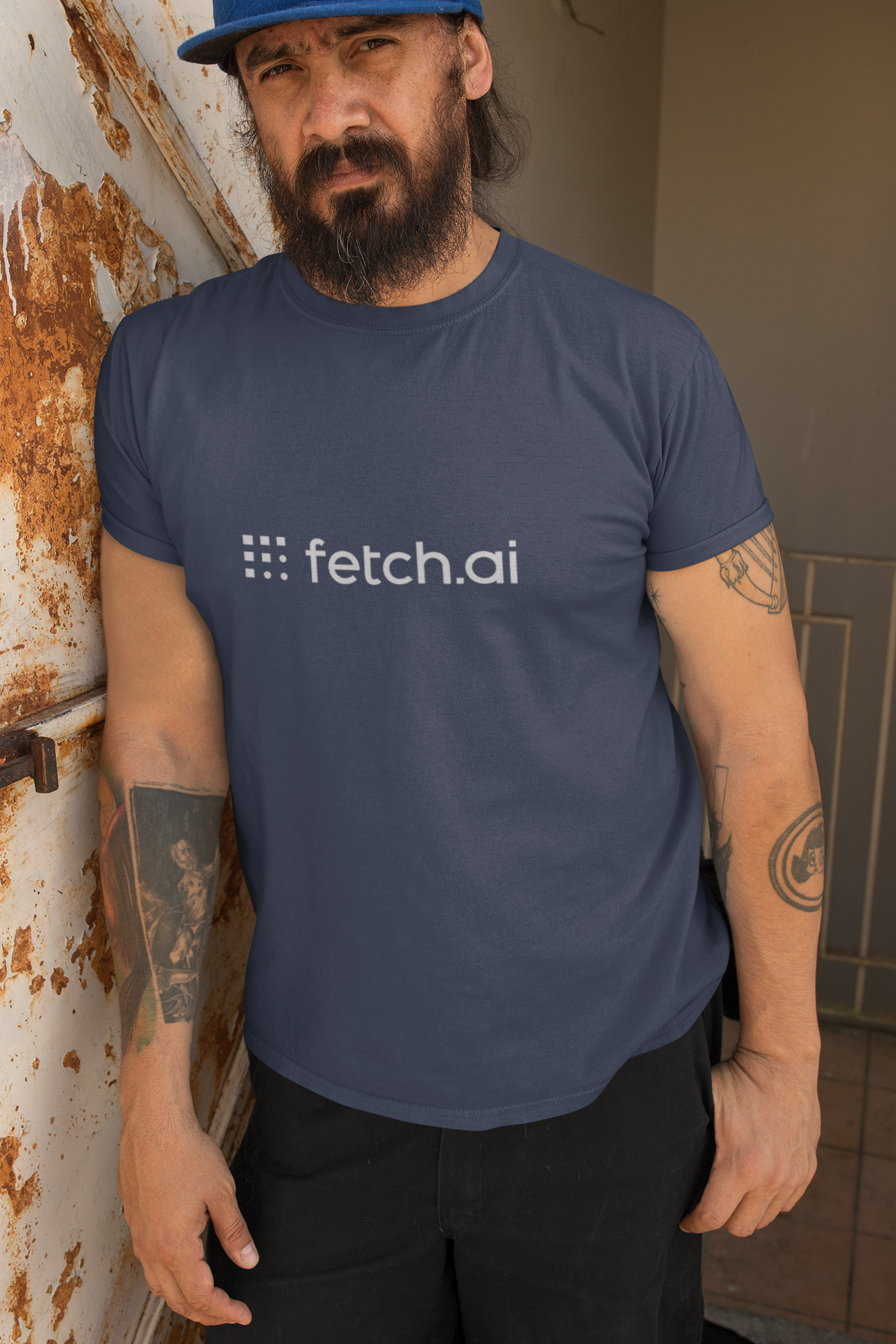 Man wearing a blue 'fetch.ai' t-shirt leaning against a wall.