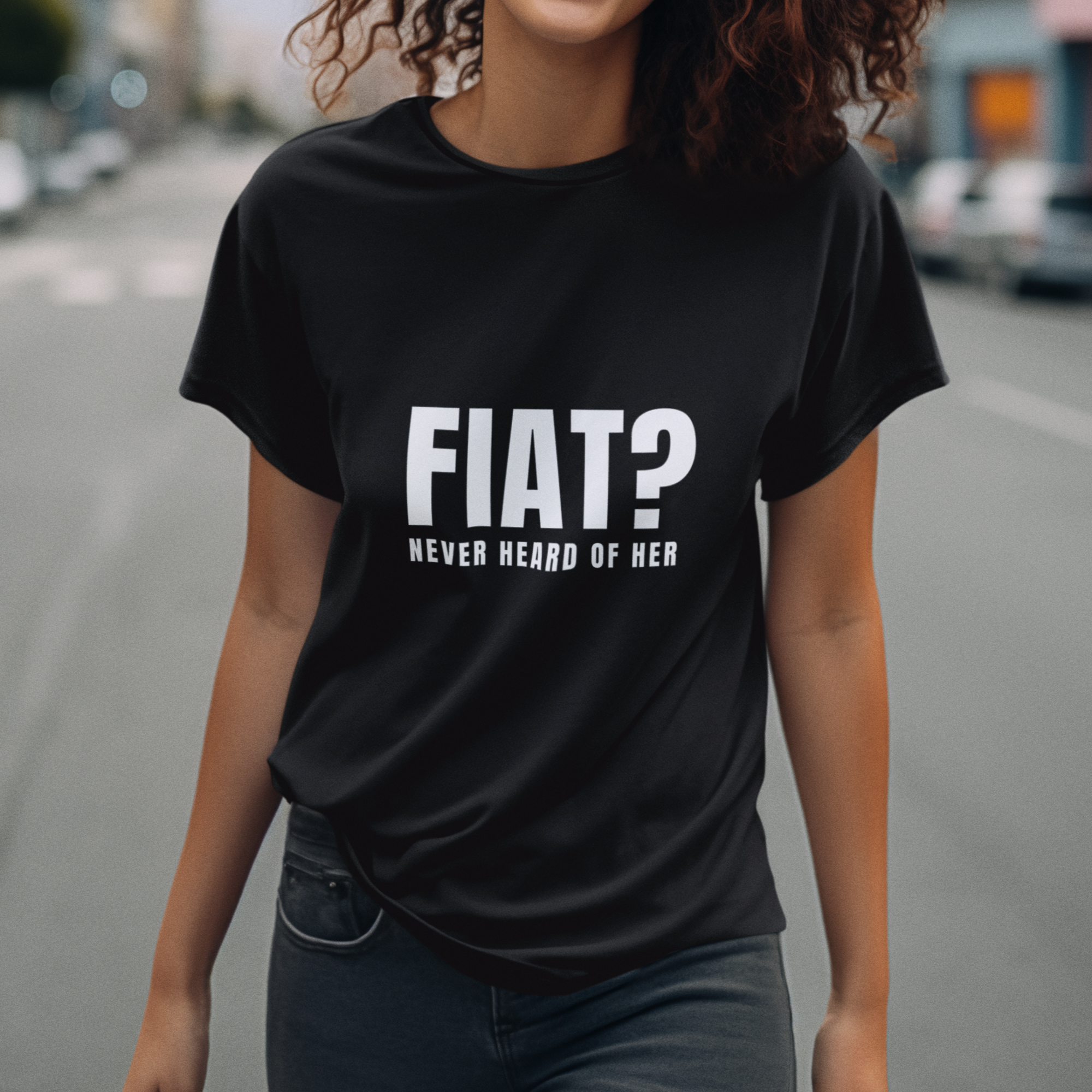 Person wearing a black t-shirt with 'FIAT? Never heard of her' text on a street.