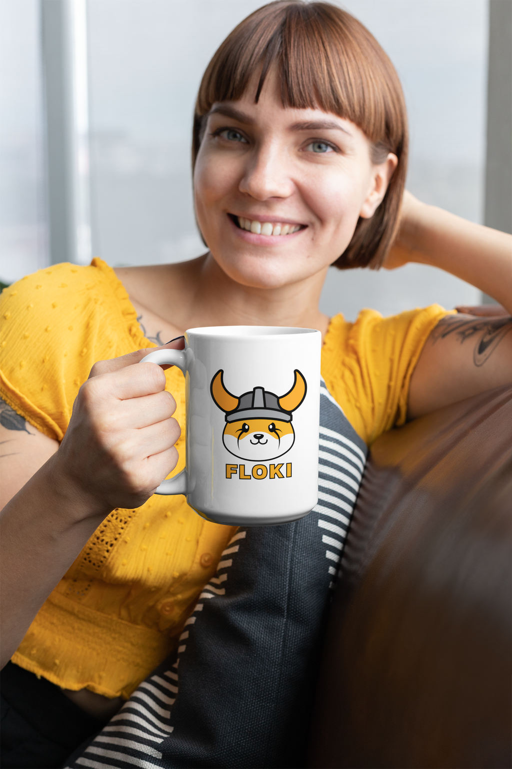 Woman holding a mug with a cartoon character and 'FLOKI!' text, wearing a yellow shirt.
