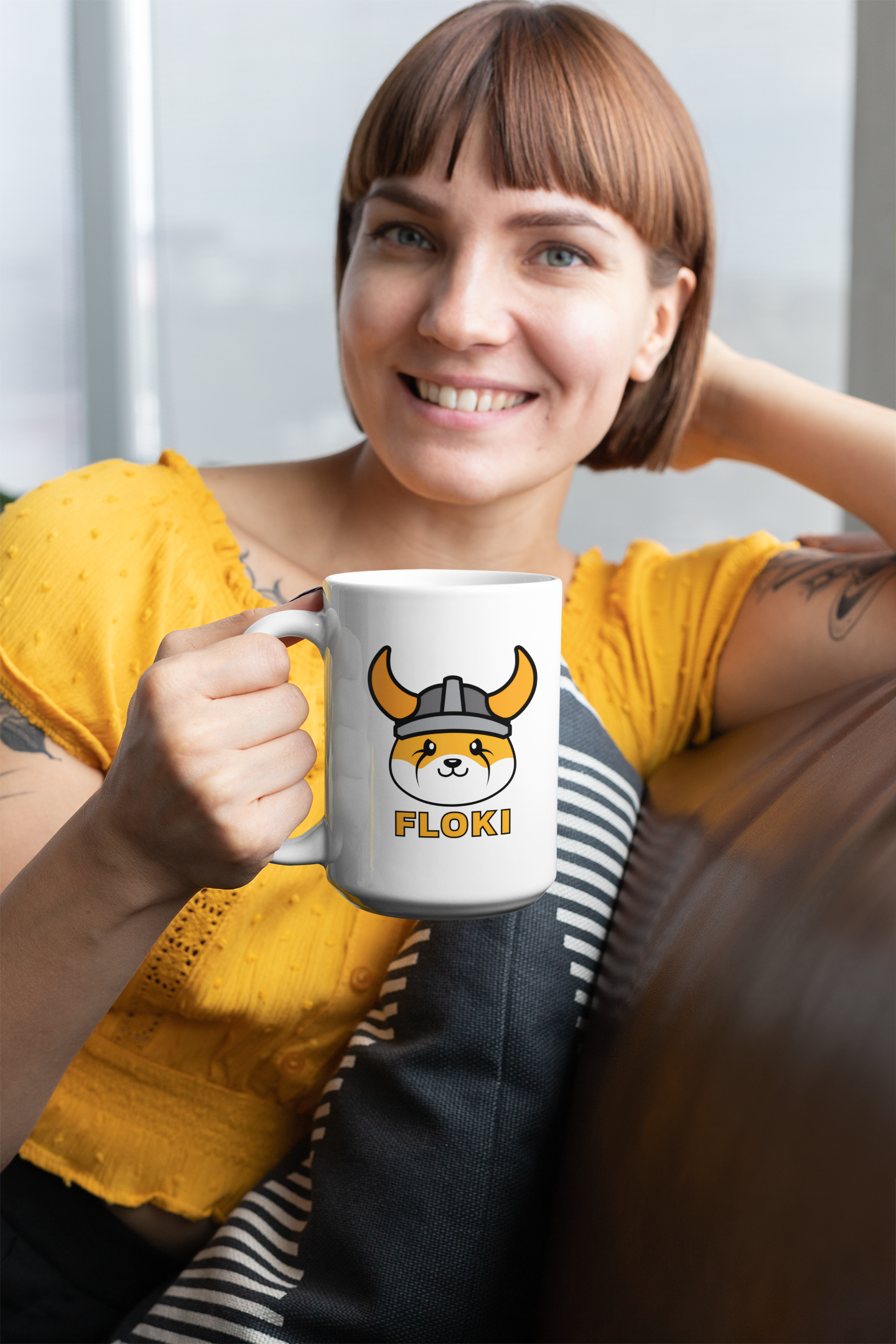 Woman holding a mug with a cartoon character and 'FLOKI!' text, wearing a yellow shirt.