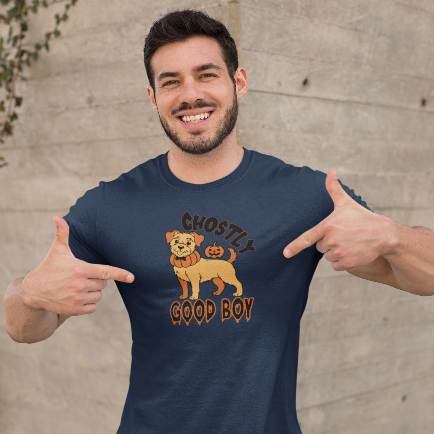 Man pointing to a navy blue t-shirt with a dog graphic and text against a concrete wall.