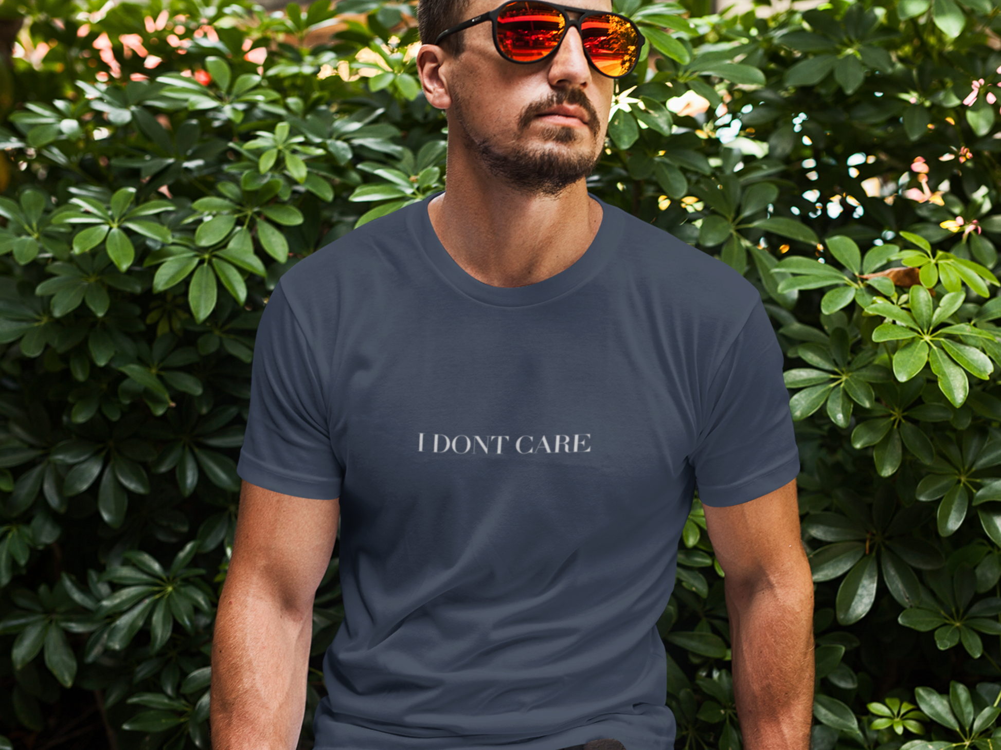 Man wearing a navy blue t-shirt with 'I DON'T CARE' text in front of green foliage.