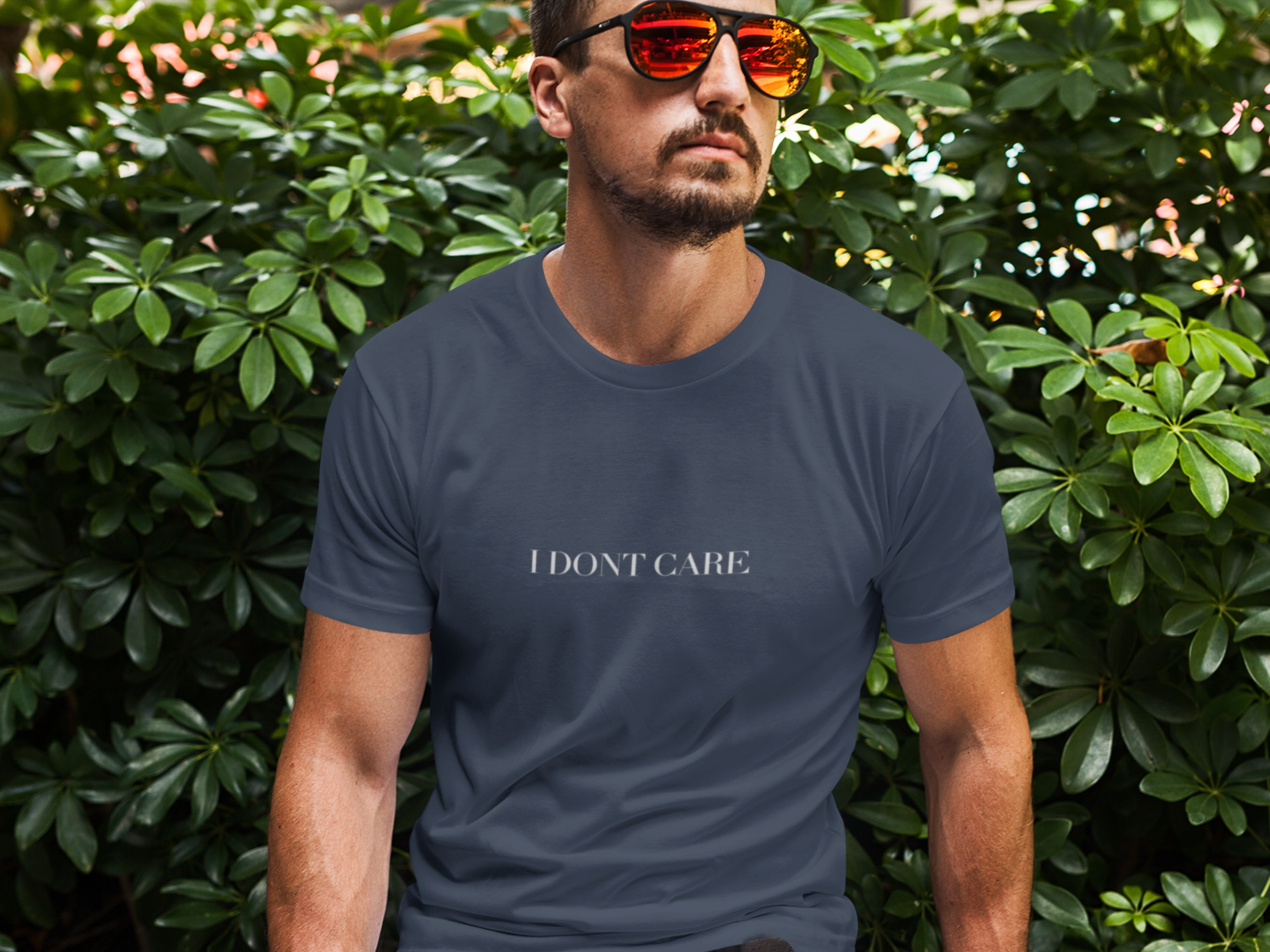 Man wearing a navy blue t-shirt with 'I DON'T CARE' text in front of green foliage.