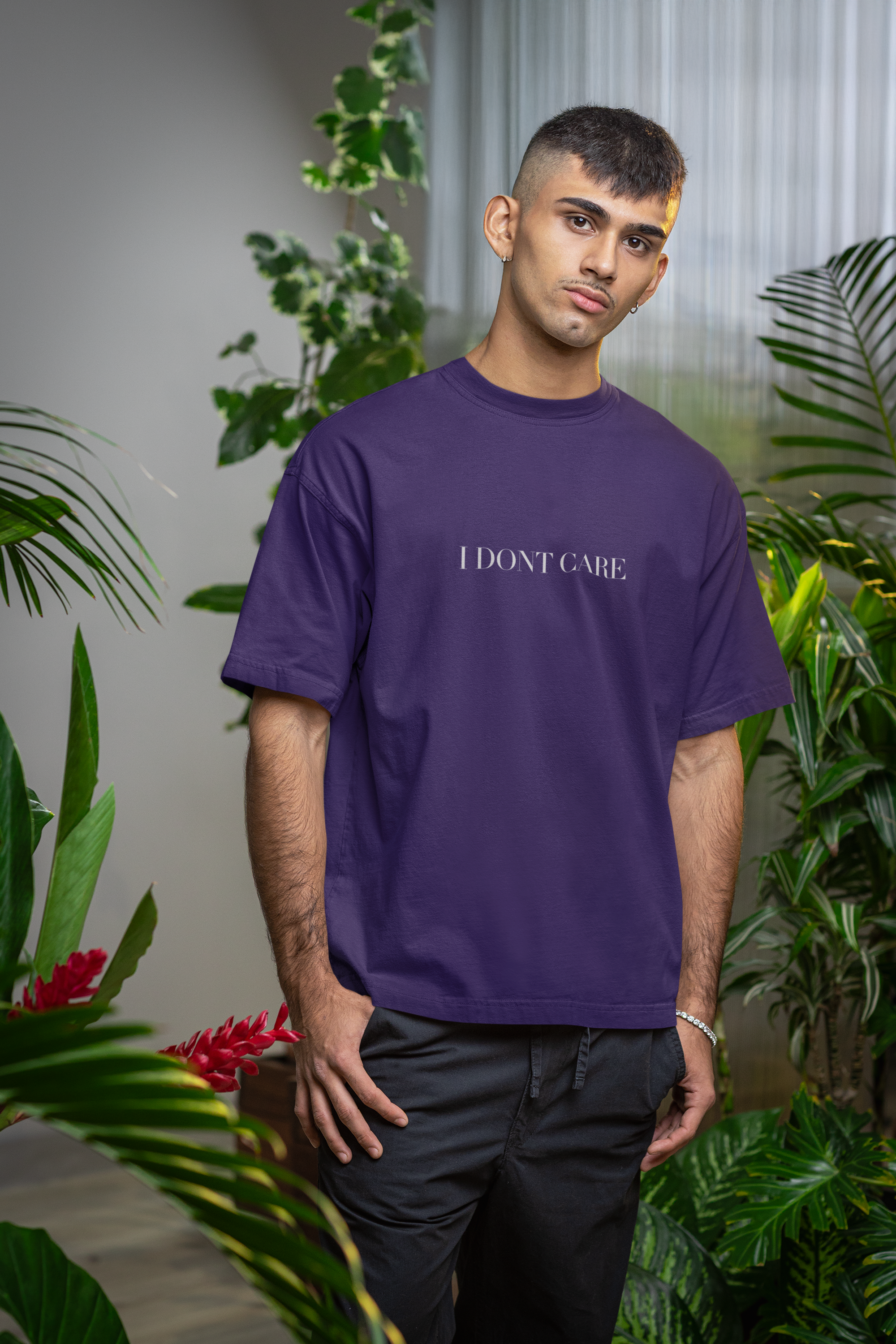 Man wearing a purple t-shirt with 'I DON'T CARE' text, standing among plants.