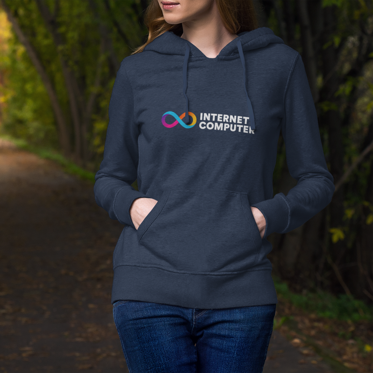 Person wearing a navy hoodie with 'Internet Computer' logo in a forest setting