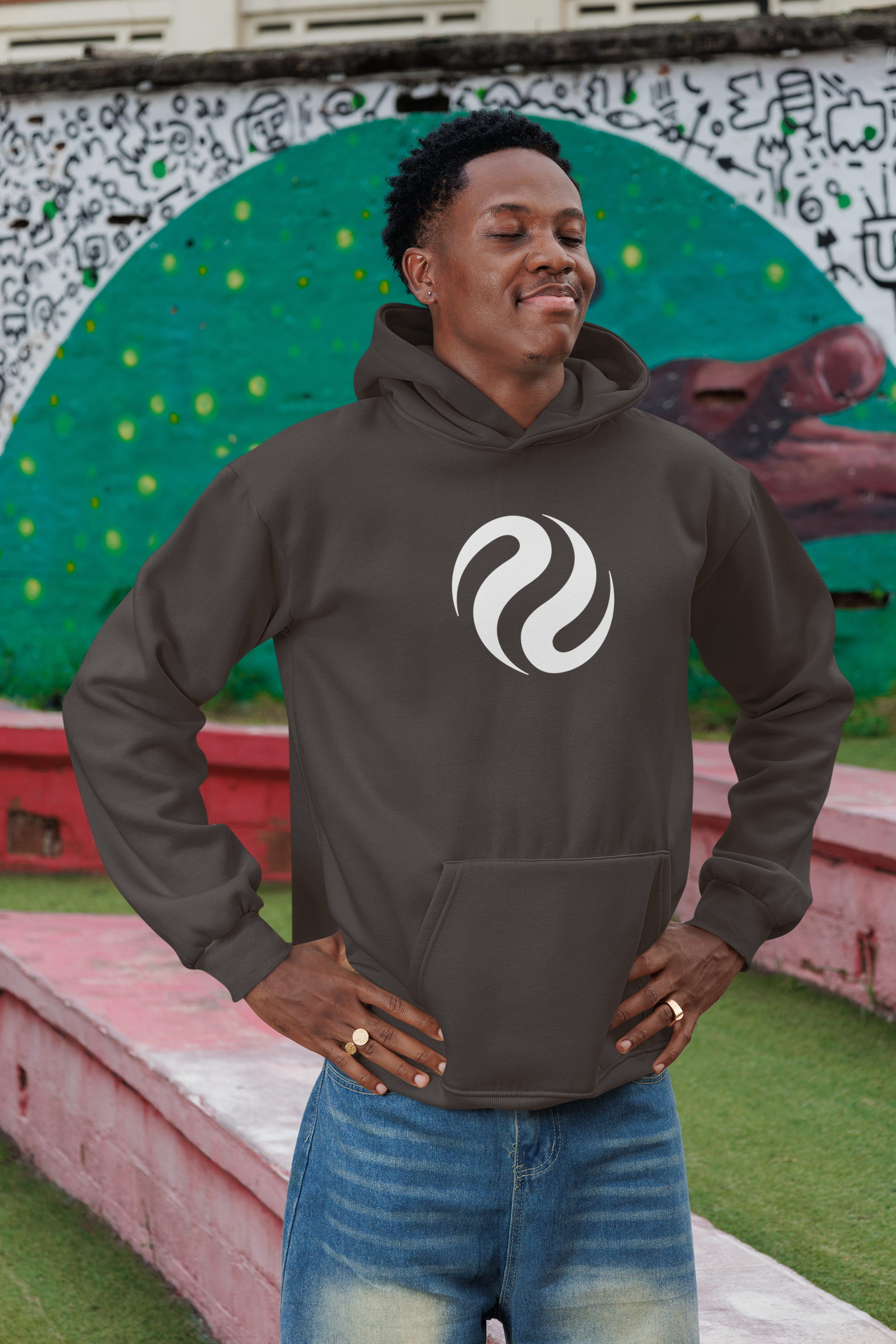 Man wearing a dark hoodie with a white logo against a colorful mural background