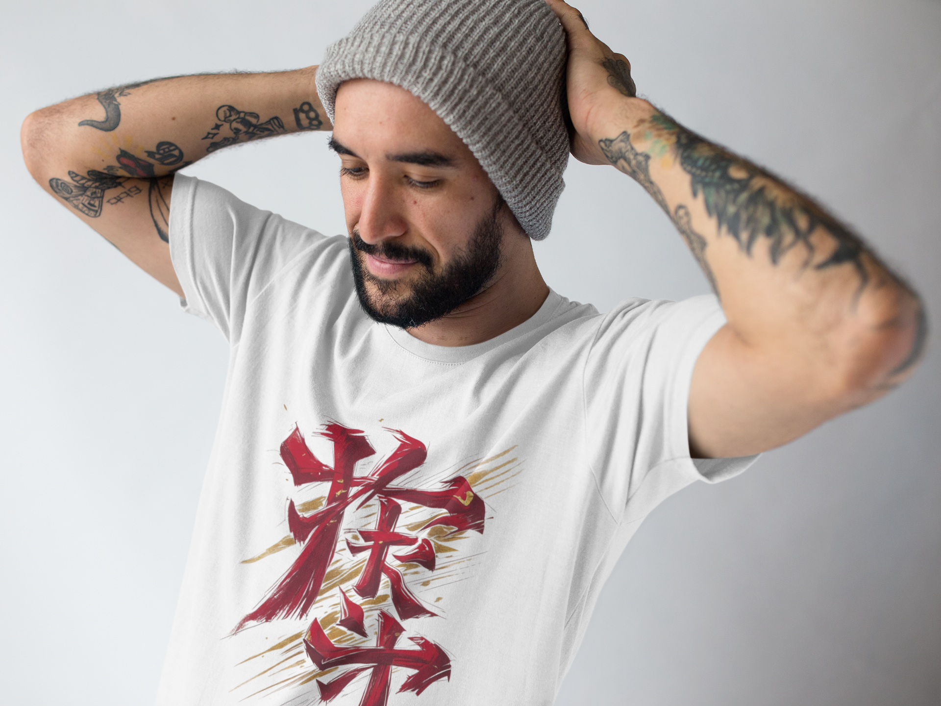 Man wearing a white t-shirt with red and gold graphic design, holding a gray beanie.