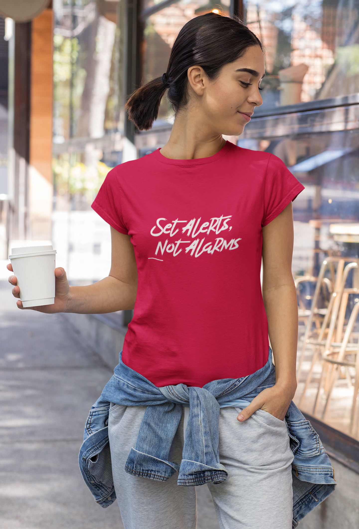 Woman wearing a red t-shirt with text, holding a cup outdoors.