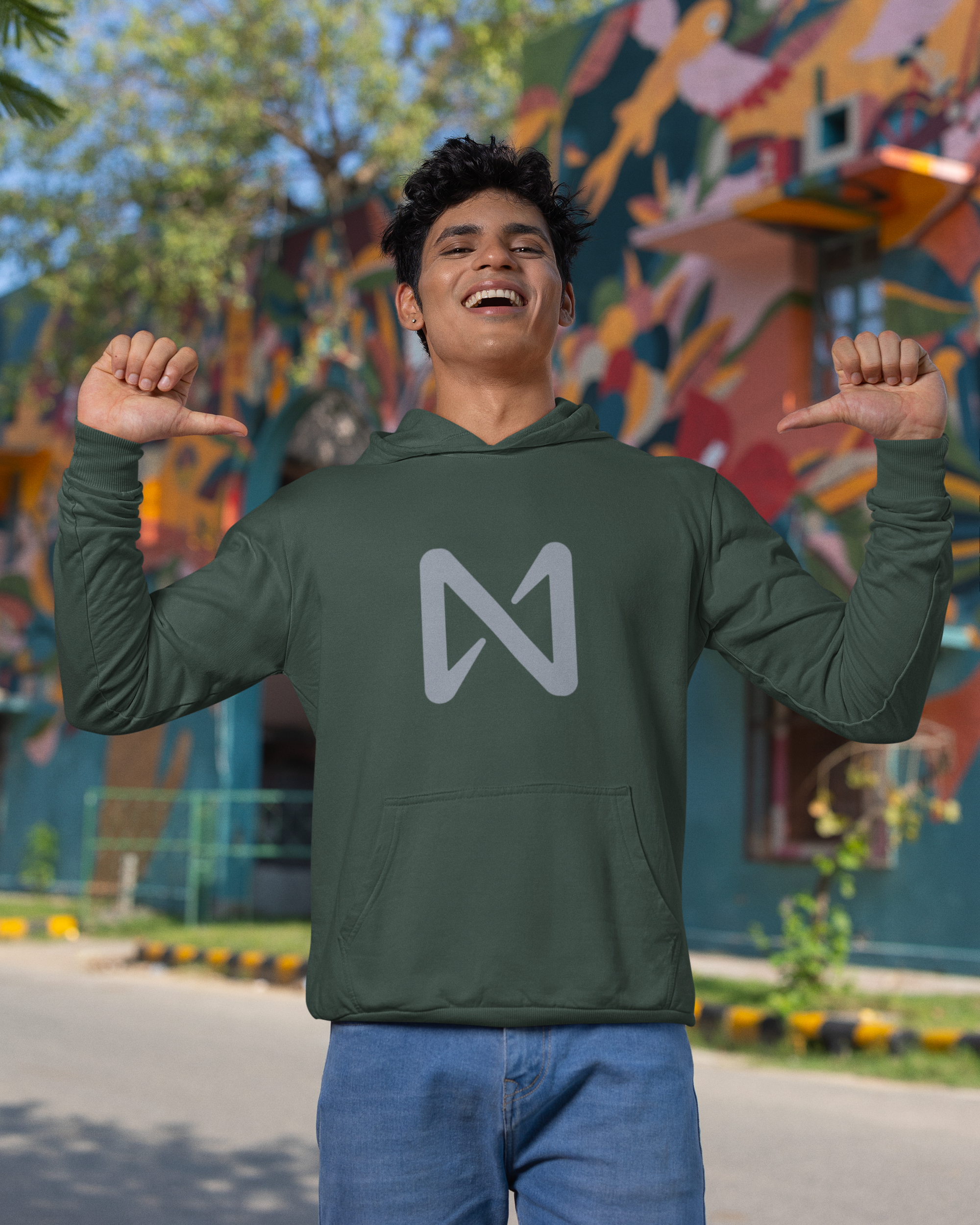 Person wearing a green hoodie with a logo, standing in front of a colorful mural.