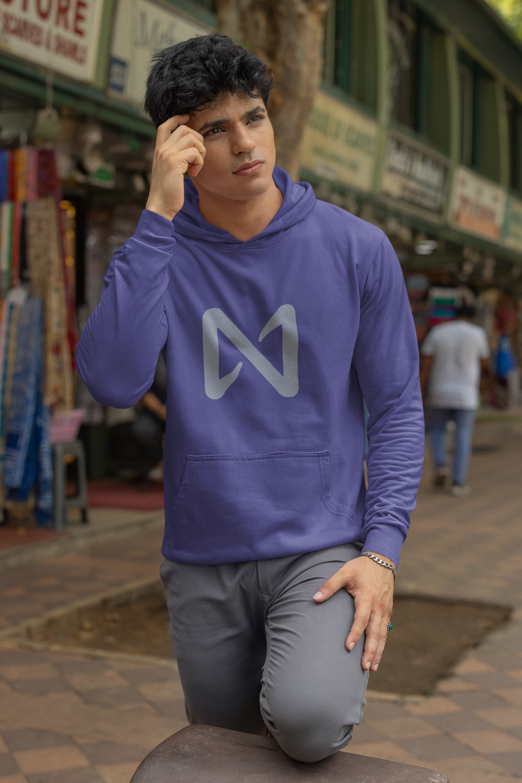 Man wearing a purple hoodie with a logo, kneeling on a street.