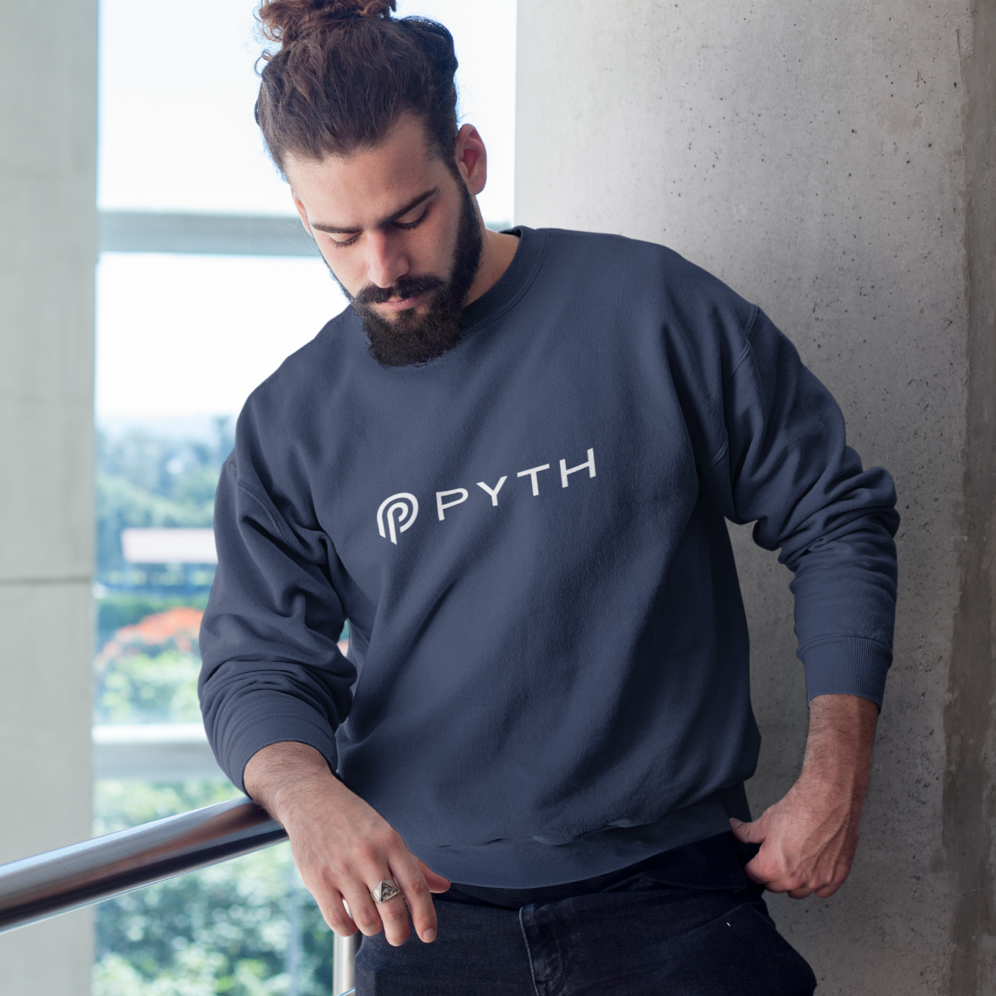 Man wearing a blue sweatshirt with 'PYTH' logo leaning against a wall.