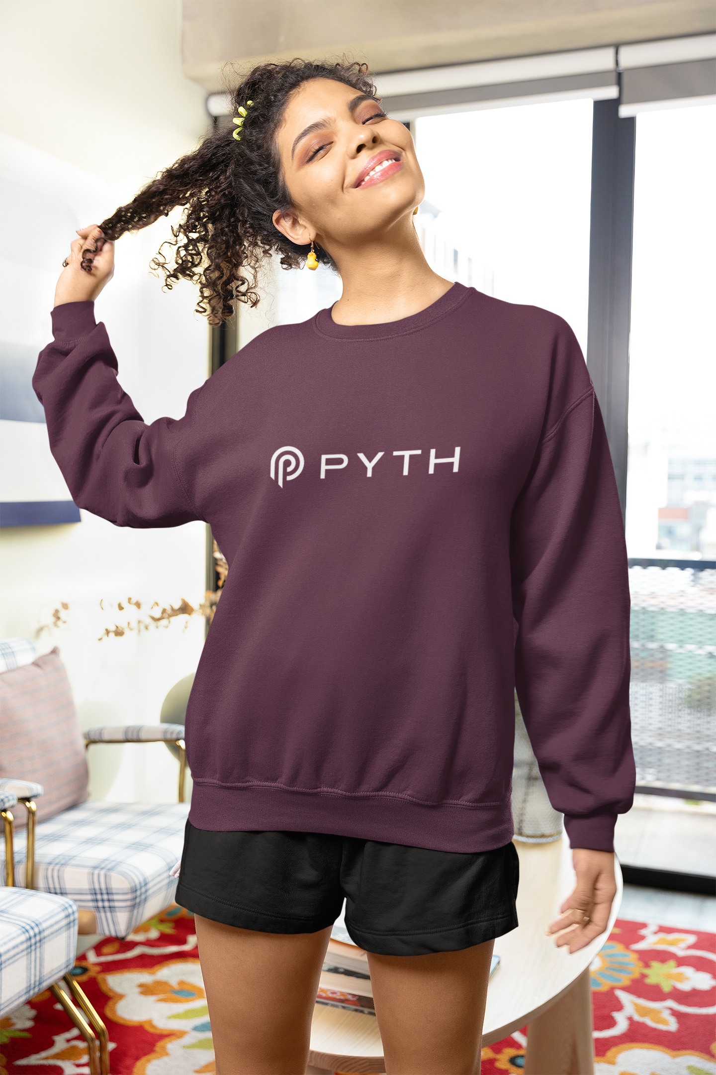 Woman wearing a purple sweatshirt with 'PYTH' logo in a living room.
