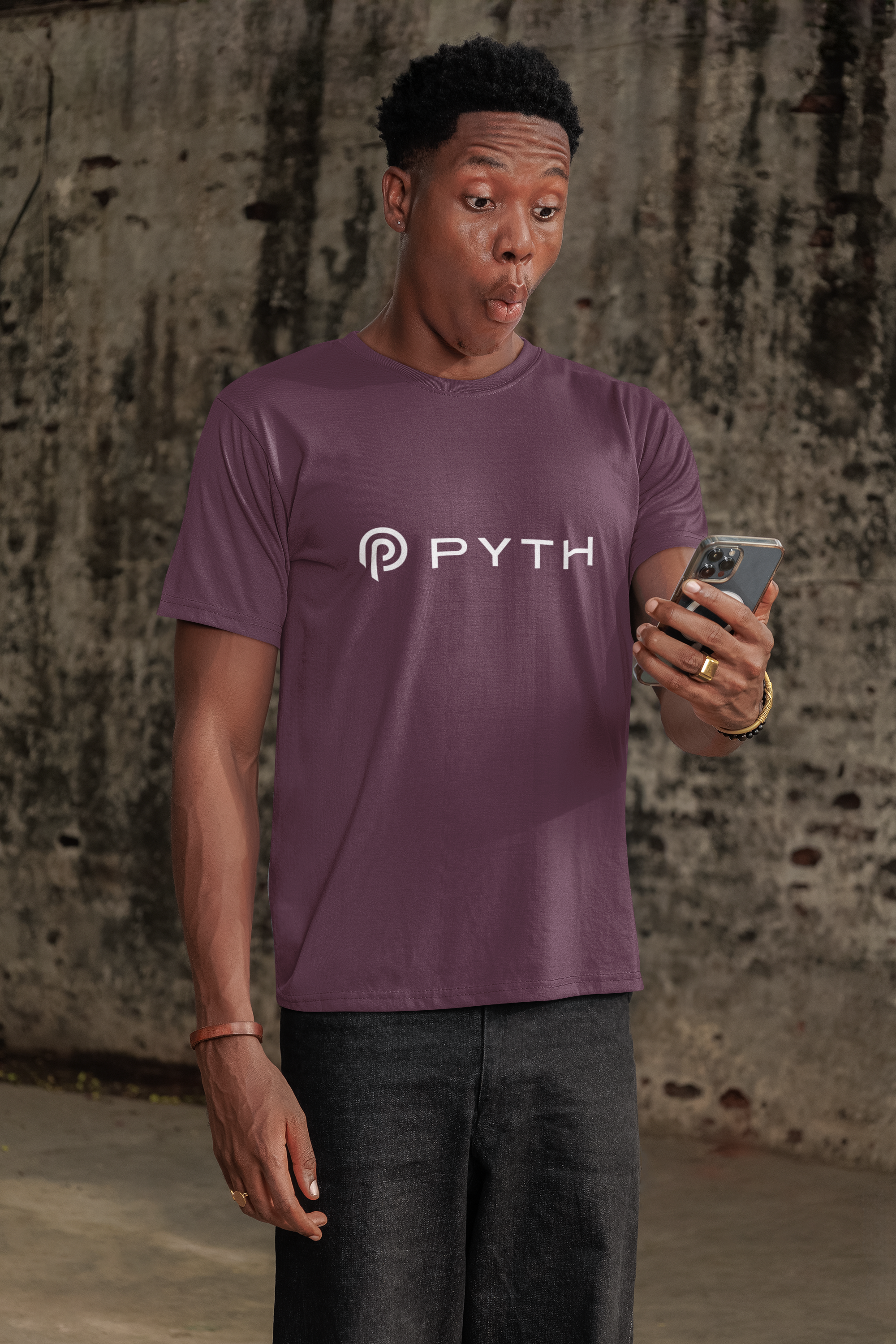 Person wearing a purple t-shirt with 'PYTH' logo, holding a phone, against a textured wall.