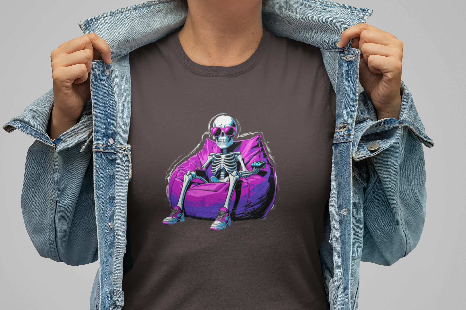 Person wearing a brown t-shirt with a colorful skeleton design, holding a denim jacket.