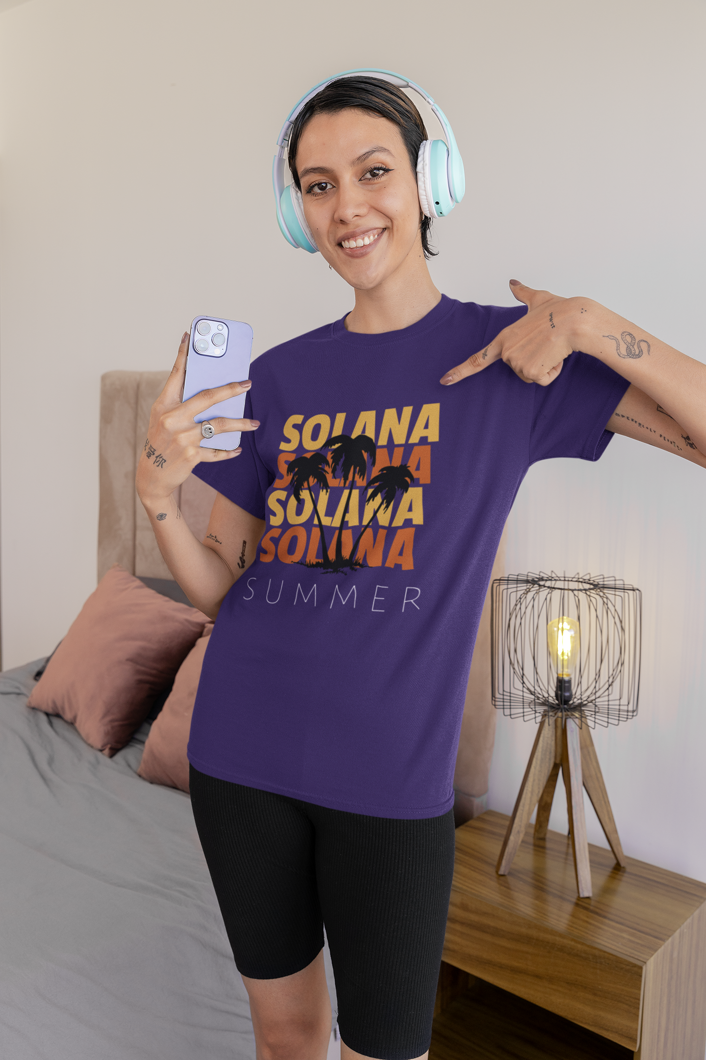 Woman wearing a purple t-shirt with 'SOLANA' text, holding a phone, in a bedroom setting.
