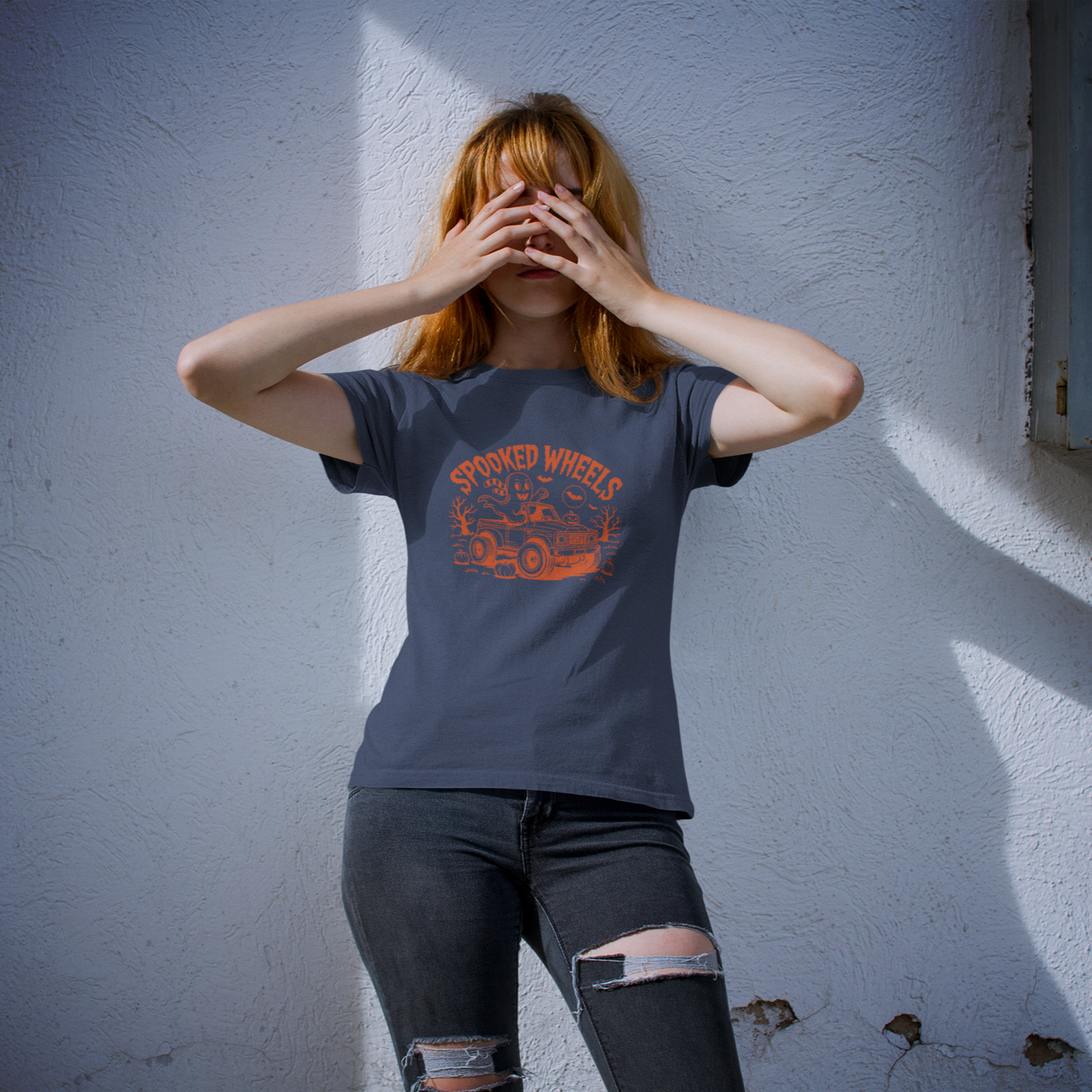 Person wearing a dark t-shirt with a graphic design, standing against a light blue wall.