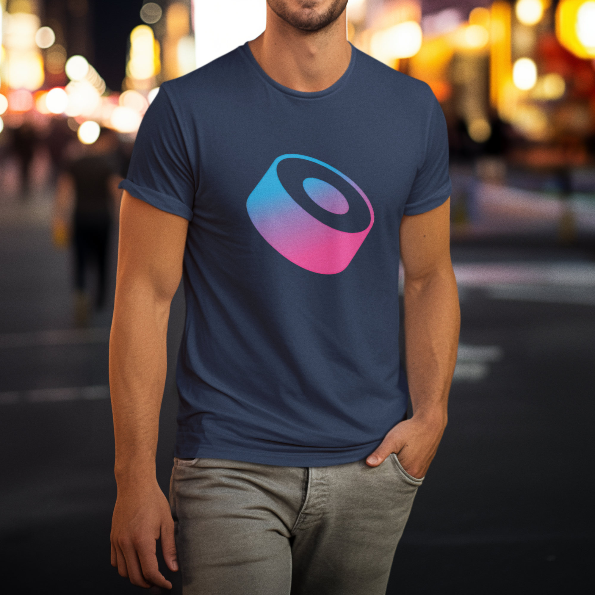 Person wearing a navy blue t-shirt with a colorful logo on a city street at night.