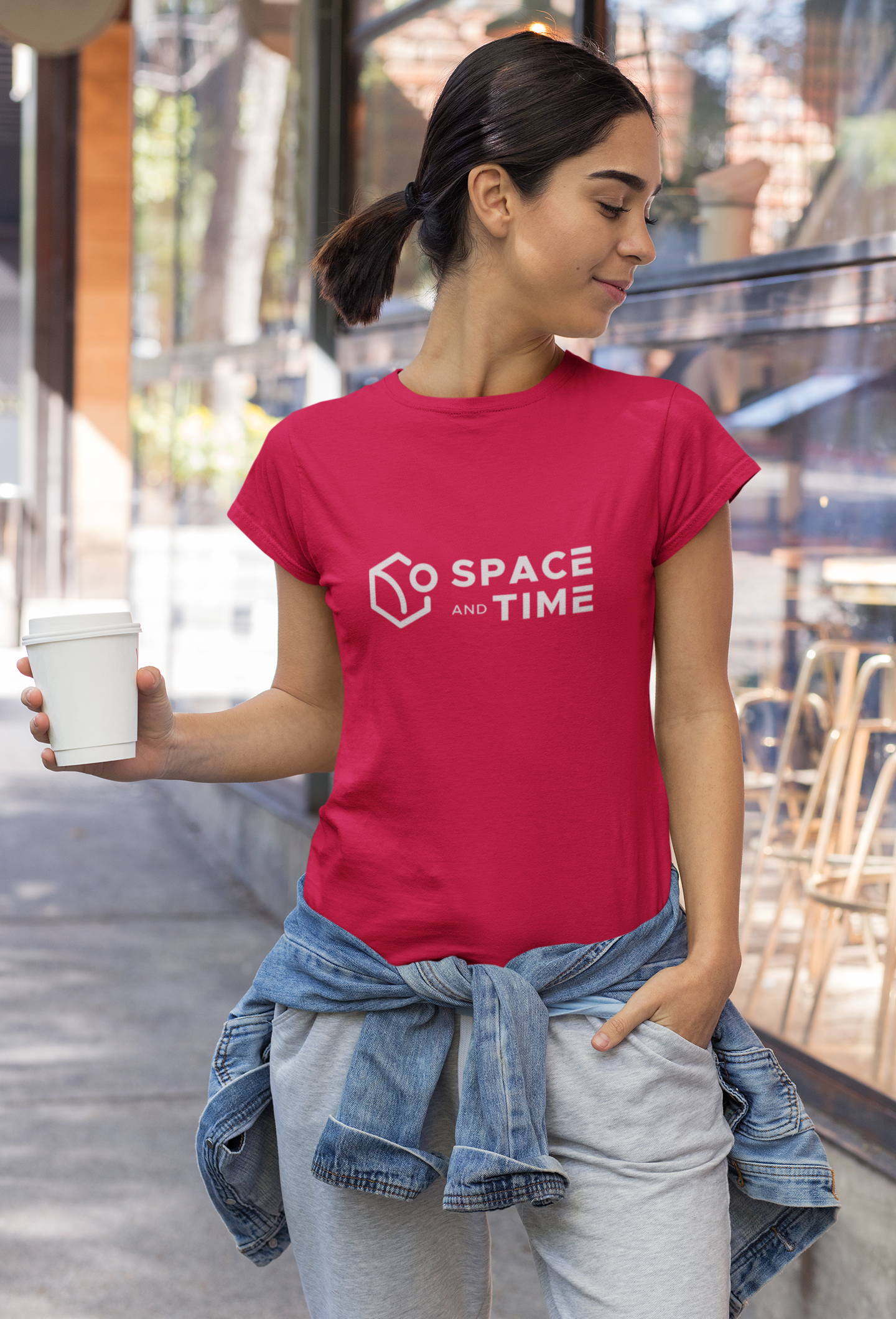Woman wearing a red t-shirt with 'Space and Time' logo, holding a cup outdoors.