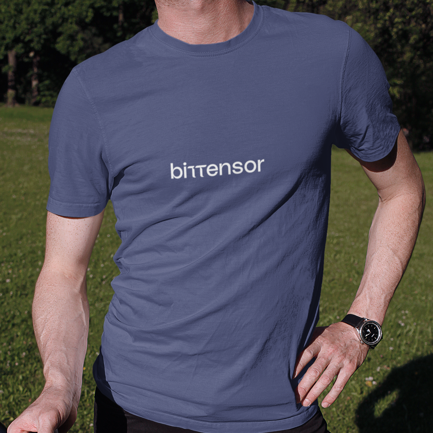 Person wearing a blue t-shirt with 'bittensor' logo, standing outdoors on grass.