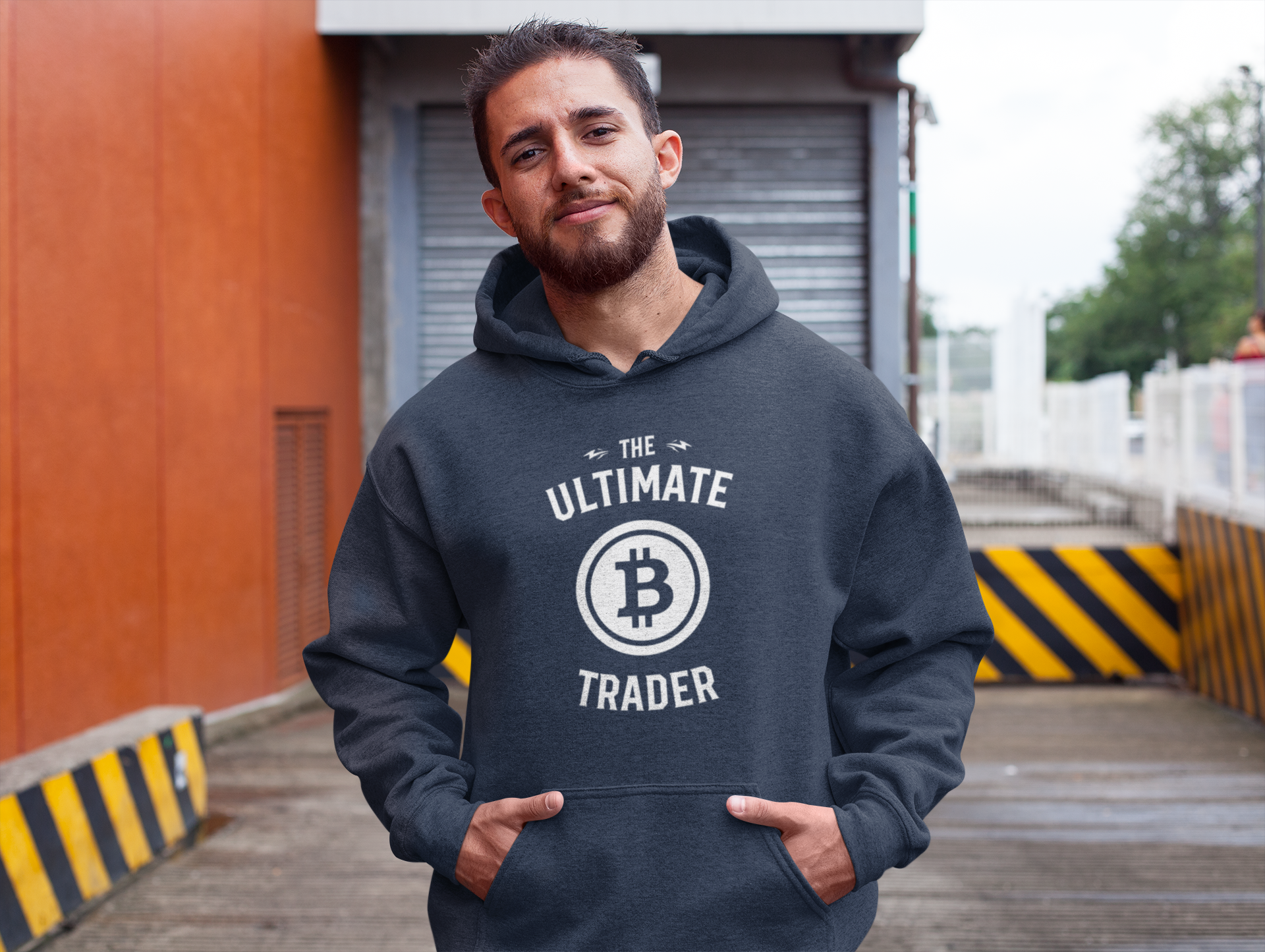 Man wearing a hoodie with 'The Ultimate Bitcoin Trader' text and logo outdoors.