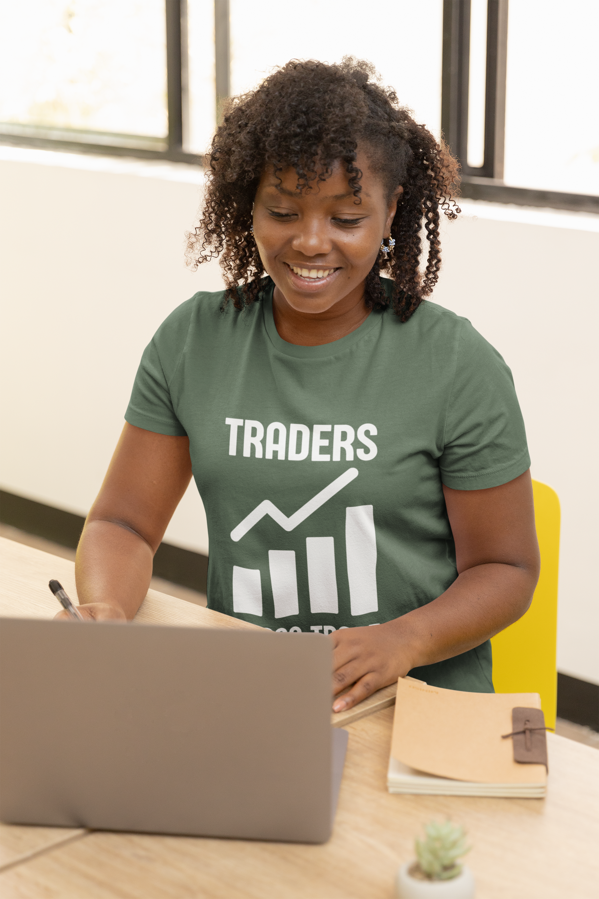 Person wearing a green 'TRADERS' t-shirt using a laptop at a desk.