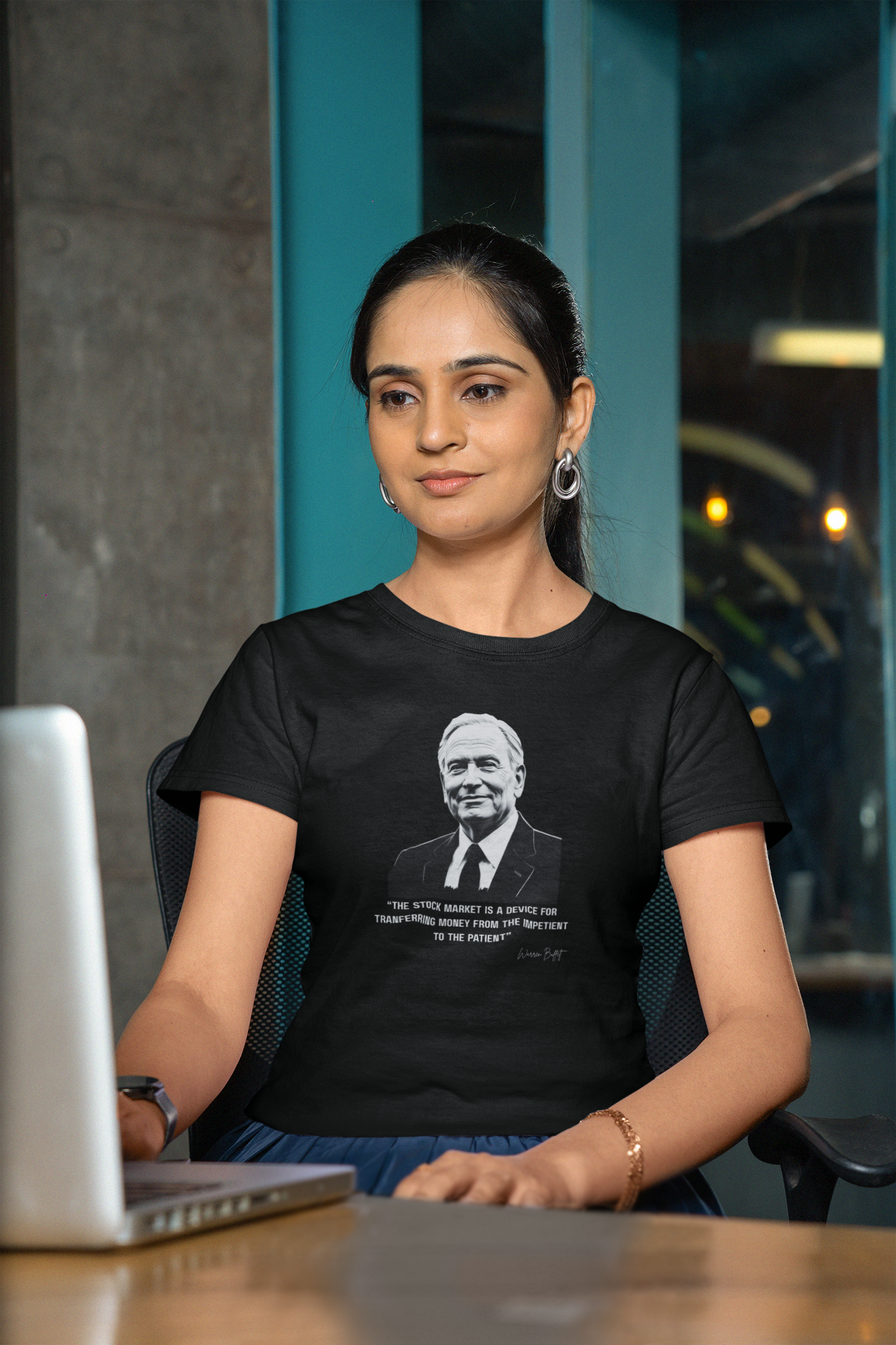 Woman wearing a black t-shirt with a printed design, sitting at a desk with a laptop.