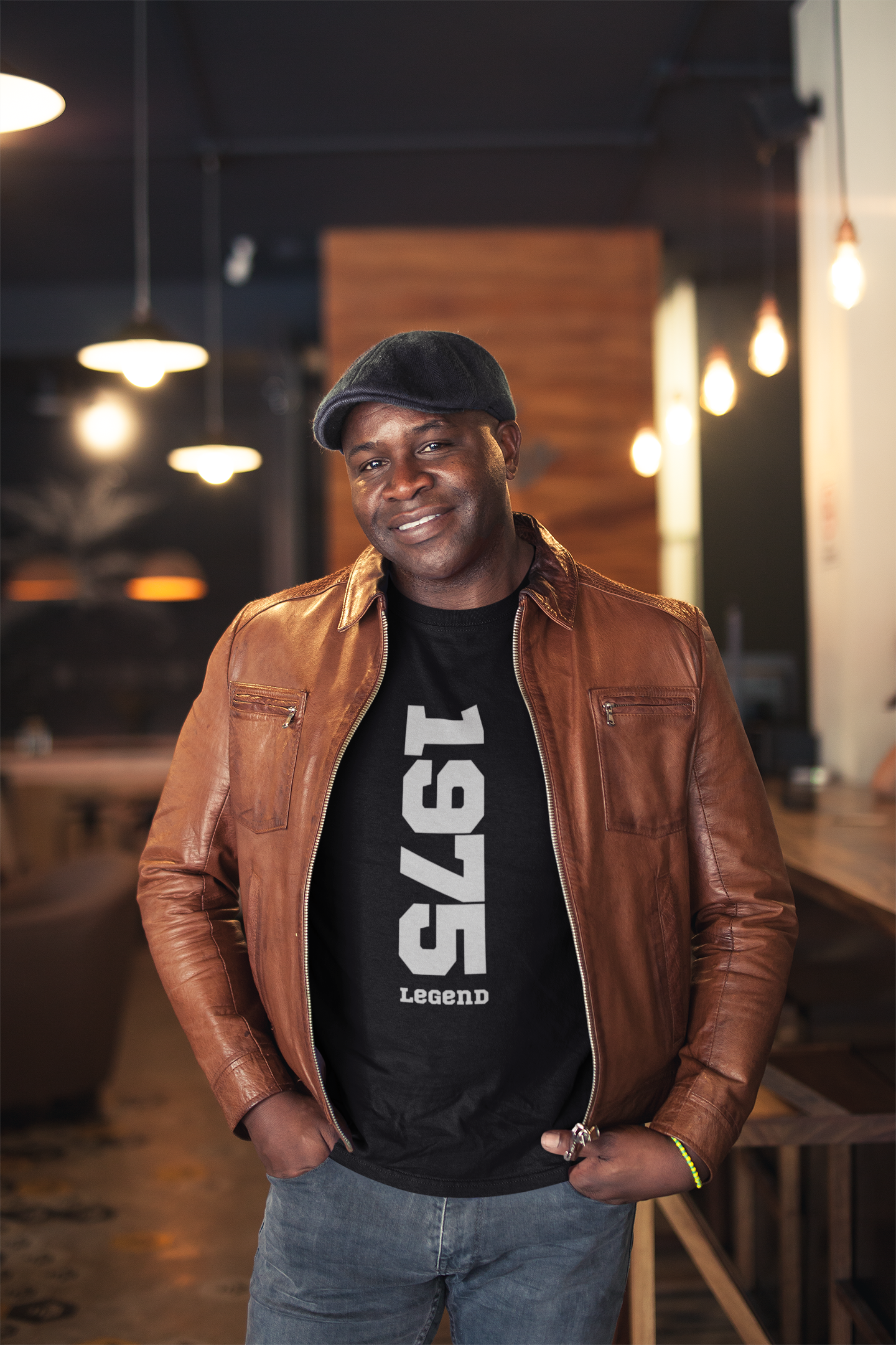 Man wearing a brown leather jacket and black t-shirt with '1975 Legend' text in an indoor setting.