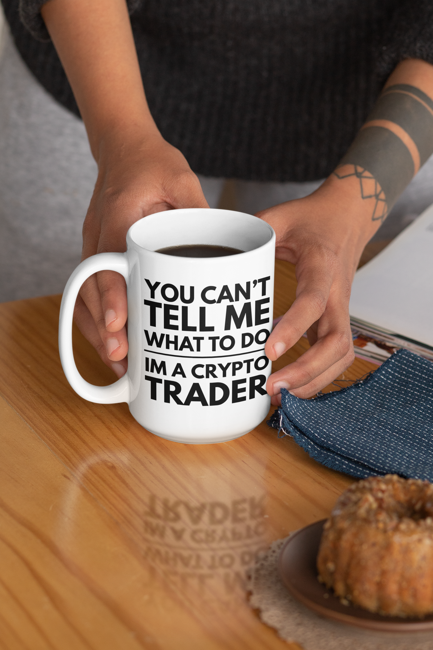 Person holding a mug with text 'You can't tell me what to do, I'm a crypto trader' on a wooden table.