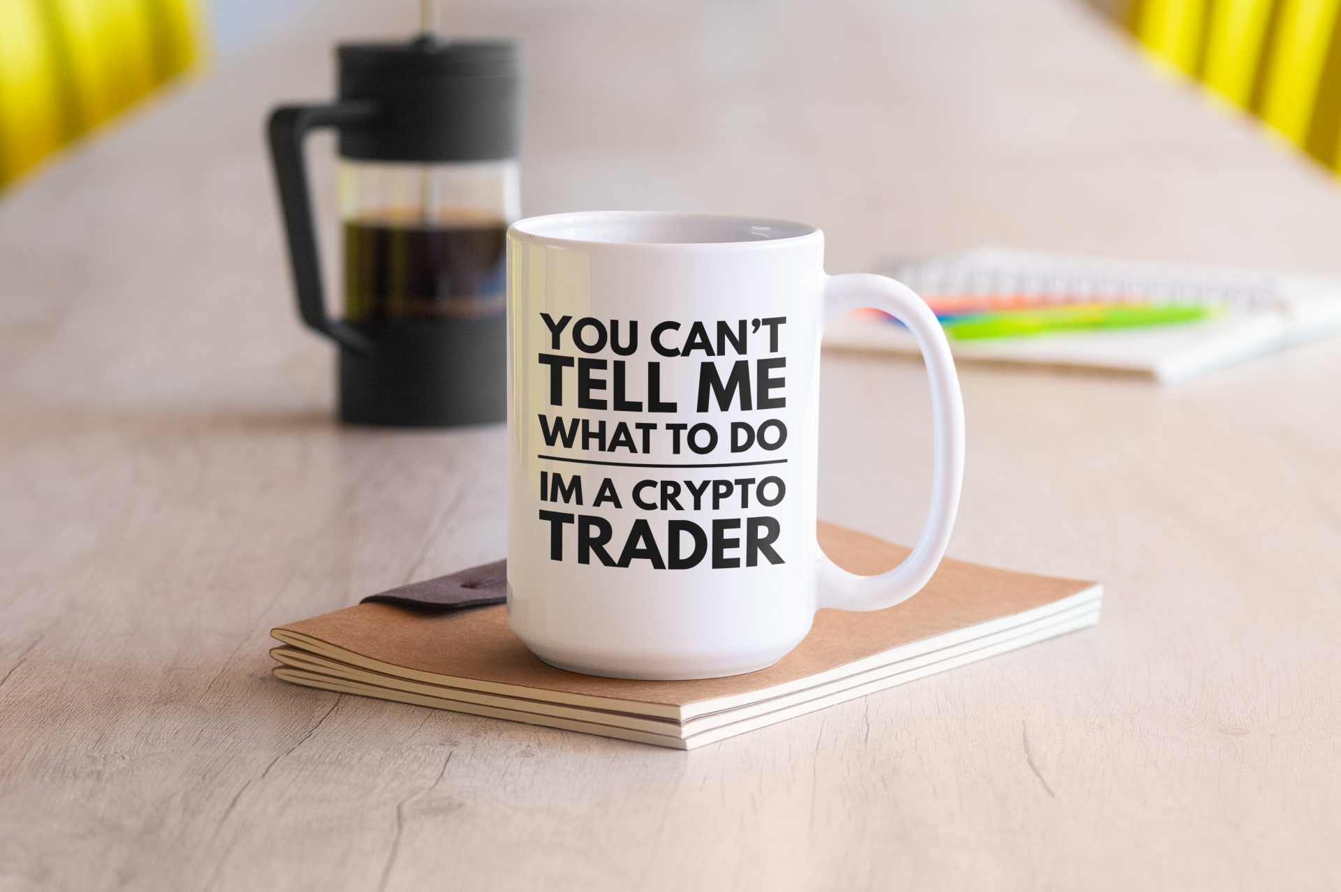 White mug with text on a wooden table with a coffee press and notebook in the background